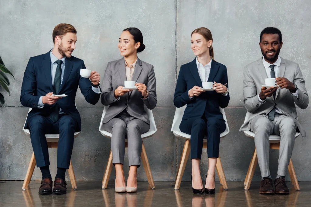 Professionals with coffee in a waiting area at a recruitment office before interviews.